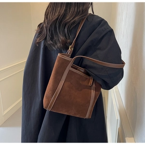 Detailed view of brown suede tote bag with leather straps worn over a winter coat