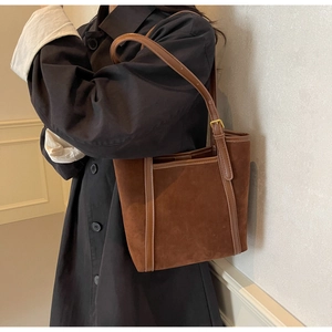 Close-up of brown suede tote bag featuring leather straps and golden metal buckle