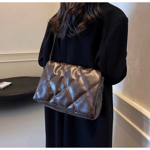 Detail of dark brown quilted crossbody bag shown on a model in a modern interior setting