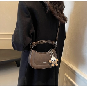 Detail einer dunkelbraunen Satteltasche mit geflochtenem Griff und Plüschanhänger