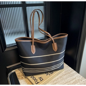 Detail of canvas tote bag with striped pattern, brown leather handles and shoulder strap