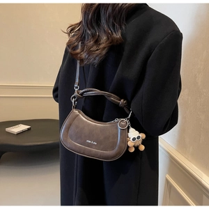 Detail einer braunen Satteltasche aus Leder mit gedrehtem Griff und Plüschbär-Anhänger