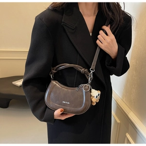 Detail der braunen Satteltasche mit Knotengriff und Bärenanhänger auf schwarzem Blazer