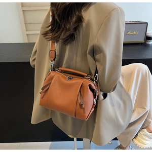 Detail of caramel brown pebbled leather Boston bag with wide strap on a model shoulder