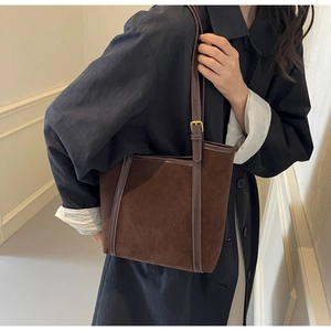 Close-up of brown suede tote bag with leather strap and gold buckle on a model