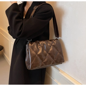Close-up of brown quilted faux leather crossbody bag texture and metallic buckles