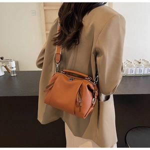 Brown lychee leather pillow bag with wide shoulder strap shown on a model's shoulder