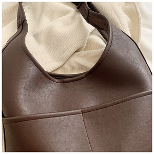 Close-up of deep brown leather shoulder bag featuring fine stitching and outer pocket detail