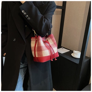 Détail d'un sac seau pied-de-poule rouge et blanc avec cordon en cuir et boucles dorées