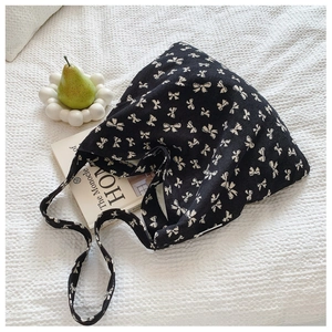 Close-up of black canvas hobo bag with white bow pattern on textured white fabric