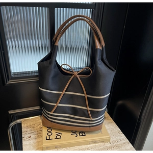 Detail of navy striped canvas tote bag with brown leather accents and bow on stone surface