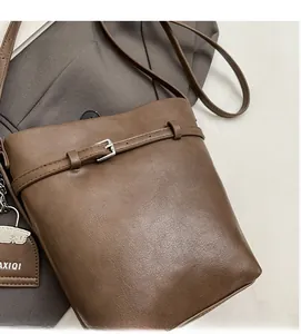 Detail of brown leather bucket bag showing soft texture and metal buckle accents