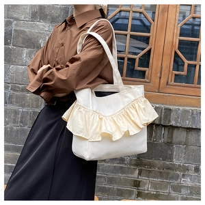 Side view of a creamy canvas tote bag with ruffle pleats carried by a model outdoors