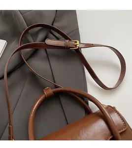 Detailed close-up of a brown leather handbag with adjustable strap and gold metal hardware
