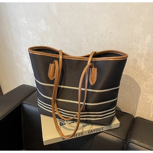 Detail of a large black canvas tote bag with white stripes and brown leather handles