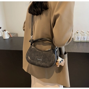 Details der grauen matten Satteltasche mit Plüschanhänger in gemütlicher Café-Atmosphäre