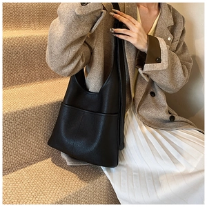 Detail of minimalist black leather tote bag with exterior pocket shown on a model