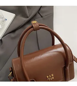 Detail of dark brown leather handbag with gold metal logo and dual comfortable handles
