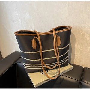 Detail of striped canvas tote bag with brown leather handles on a leather sofa