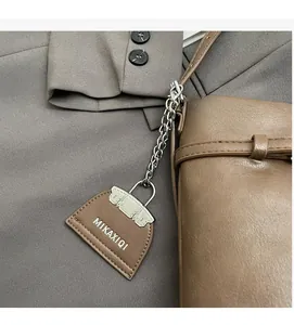 Detail view of brown matte leather bucket bag with a miniature logo charm and silver chain