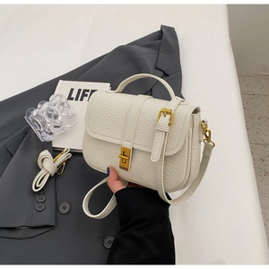 Detail of white textured leather handbag featuring golden twist-lock and adjustable strap