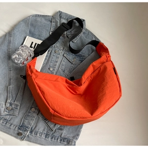 Detail view of bright orange crescent crossbody bag made of textured nylon with strap