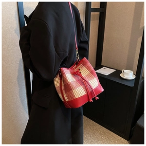 Détail d'un sac seau à carreaux rouges avec cordon porté sur un manteau noir