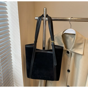 Detail of a black suede tote bag hanging with a trench coat showing golden hardware