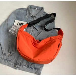 Bright orange nylon crescent crossbody bag on denim jacket with adjustable strap
