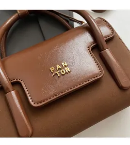 Macro shot of dark brown polished leather bag with golden PAN TOR logo and round handle