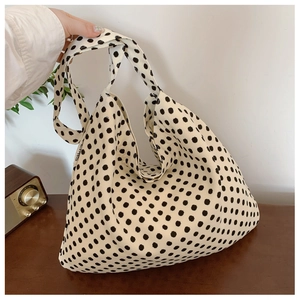 Detailed close-up of white canvas tote bag featuring black polka dots and side woven label