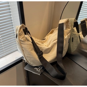 Close-up of cream nylon crescent bag with adjustable black strap and side label detail