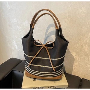 Detail of striped canvas tote bag featuring brown leather bow and sturdy dual handles