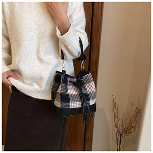 Détail d'un sac seau à carreaux britanniques avec texture tweed et finitions en cuir noir