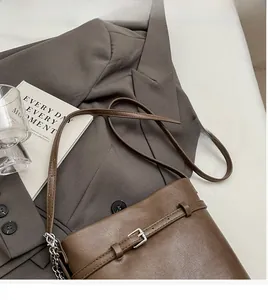 Detail view of dark brown leather bucket bag on grey suit jacket with chain strap