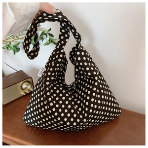 Detailed view of black canvas tote bag with white polka dots and EMIS side brand label