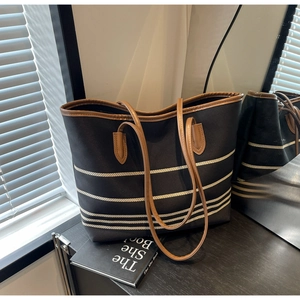 Detail of black canvas tote bag featuring white stripes and brown leather handles on wood