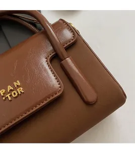 Close-up of brown textured leather flap with fine hand-stitching and gold logo