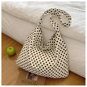 Polka dot canvas tote bag resting against a bed beside a book and green apples