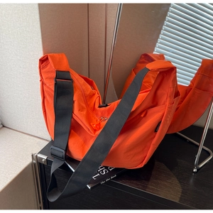 Detail of orange nylon crossbody bag with adjustable strap and side brand label