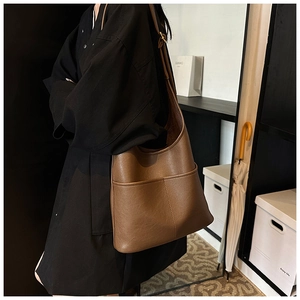 Detail view of brown leather tote bag showing the side pocket and metal strap buckle