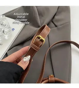 Detail of adjustable brown leather shoulder strap with gold-tone buckle on crossbody bag