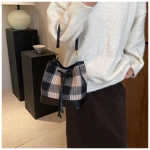 Gros plan du sac seau à carreaux avec bandoulière en cuir porté par un mannequin