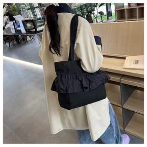Black canvas tote bag with ruffle layers shown on a shoulder in a cafe setting