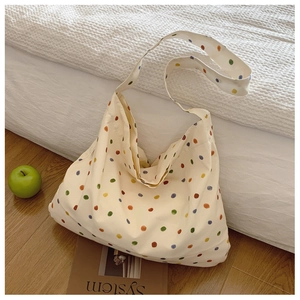 Detail view of cream canvas tote bag with multi-colored polka dots on a wooden floor