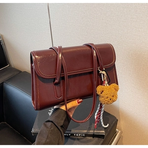 Detail of burgundy leather shoulder bag with glossy finish and cute brown bear charm