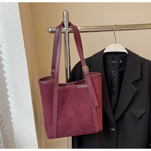 Detail of burgundy suede tote bag with adjustable thin strap and gold metal buckle