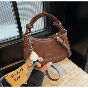 Details einer braunen Vintage-Satteltasche mit Plüschanhänger und Lederstruktur-Ansicht