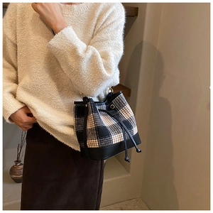 Détail du sac seau à carreaux avec cordon de serrage et base en cuir porté par un mannequin
