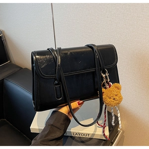 Detail of black glossy shoulder bag with pleated texture and plush bear charm